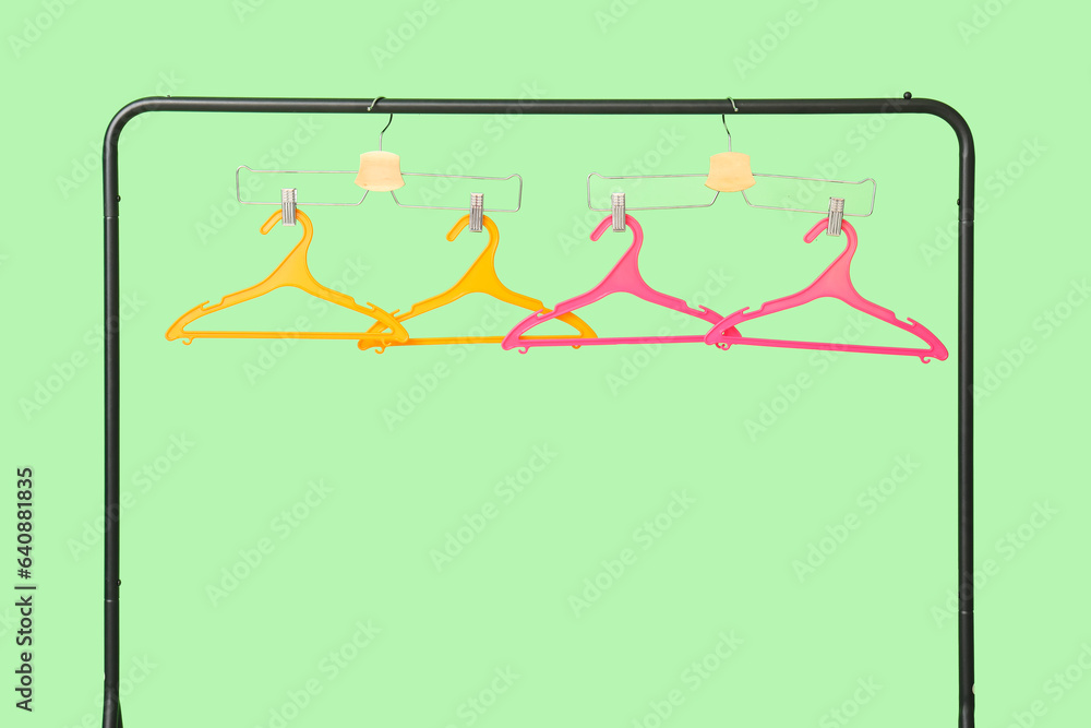 Rack with plastic clothes hangers on green background