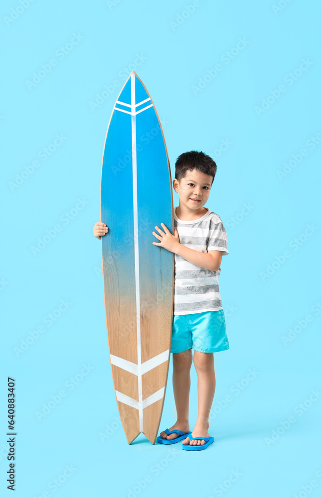 Cute little Asian boy with surfboard on blue background