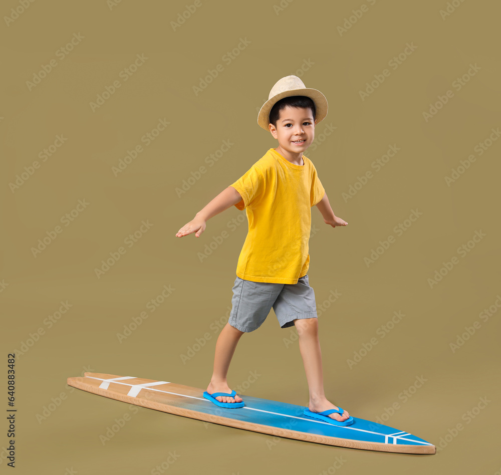 Cute little Asian boy standing on surfboard against green background