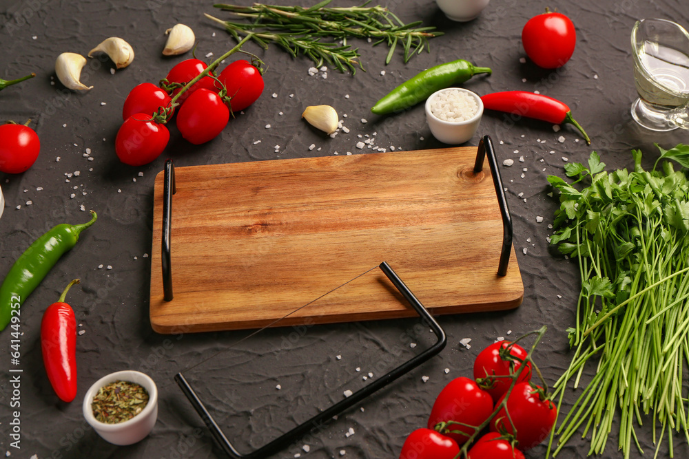 Composition with wooden kitchen board, fresh vegetables, herbs and spices on dark background
