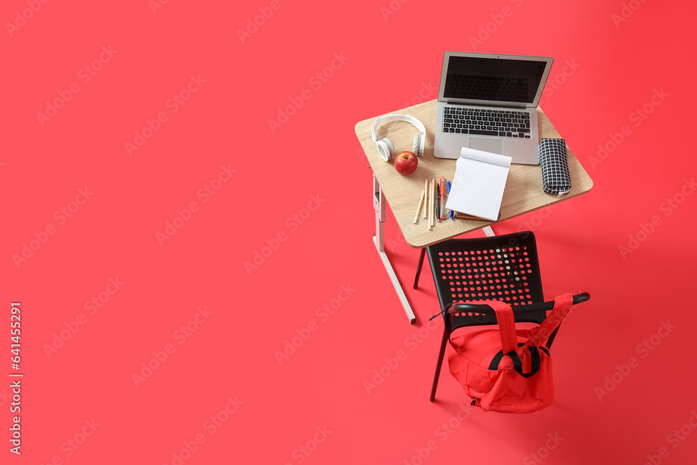 Modern school desk with laptop, headphones and stationery on red background