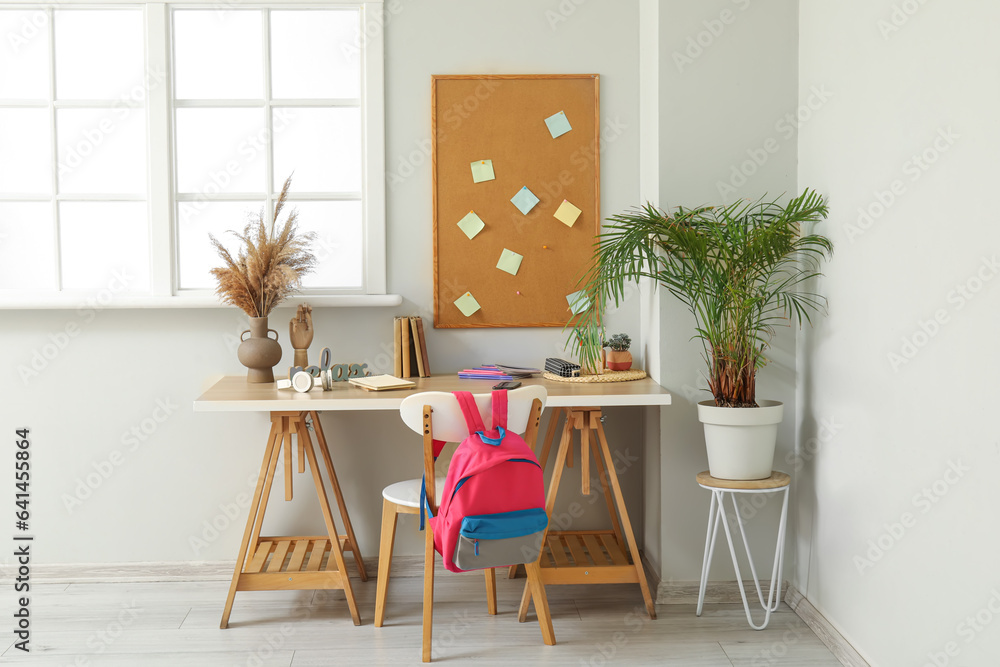 Modern school desk with stationery in room near white wall