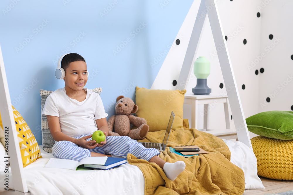 Little African-American boy with apple studying online in bedroom