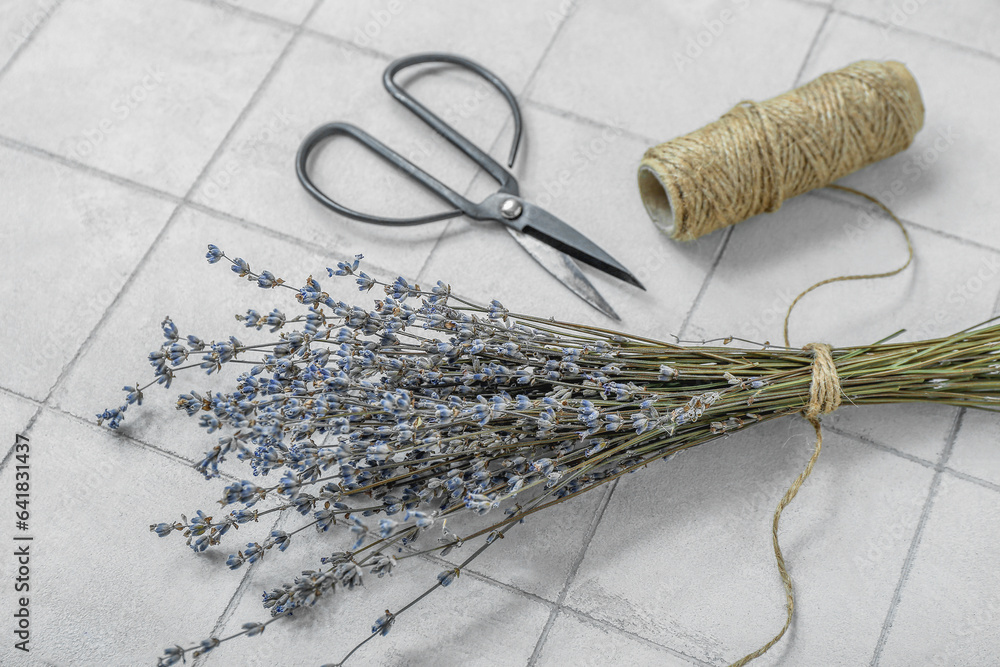 Scissors with thread and dried lavender on white tile background