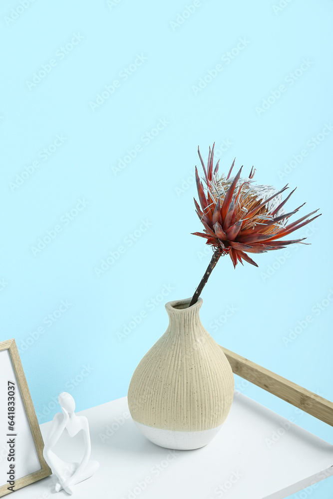 Vase with dried red protea, figurine and photo frame on shelving unit near blue wall