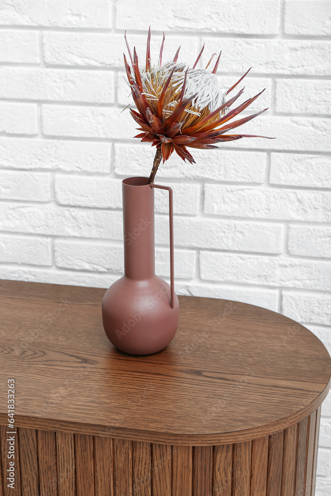 Vase with dried red protea on dresser near white brick wall