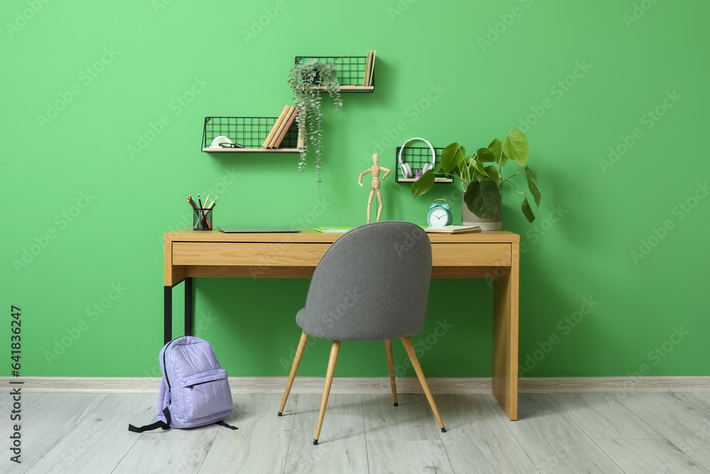 Modern school desk with laptop and stationery in room near green wall