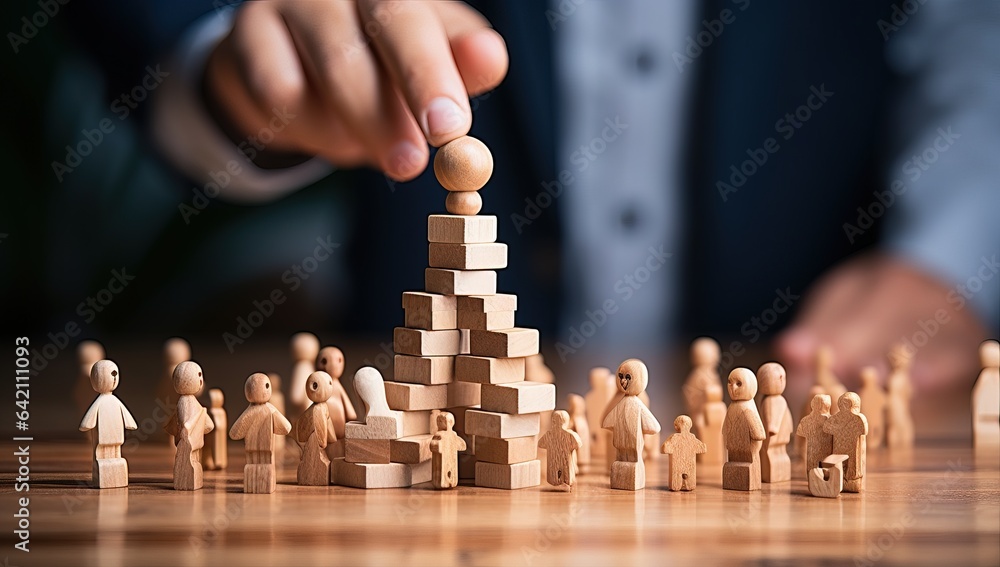Businessman hand is placing a wooden block on a pyramid of people.