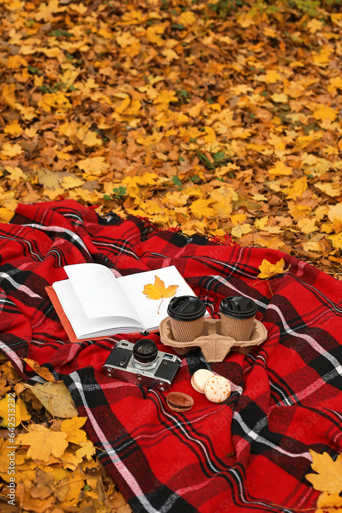 Book with autumn leaf, cups of coffee, macaroons and photo camera on plaid in park