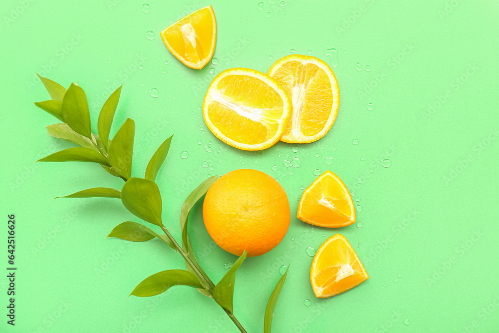 Cut orange with plant branch and water drops on green background