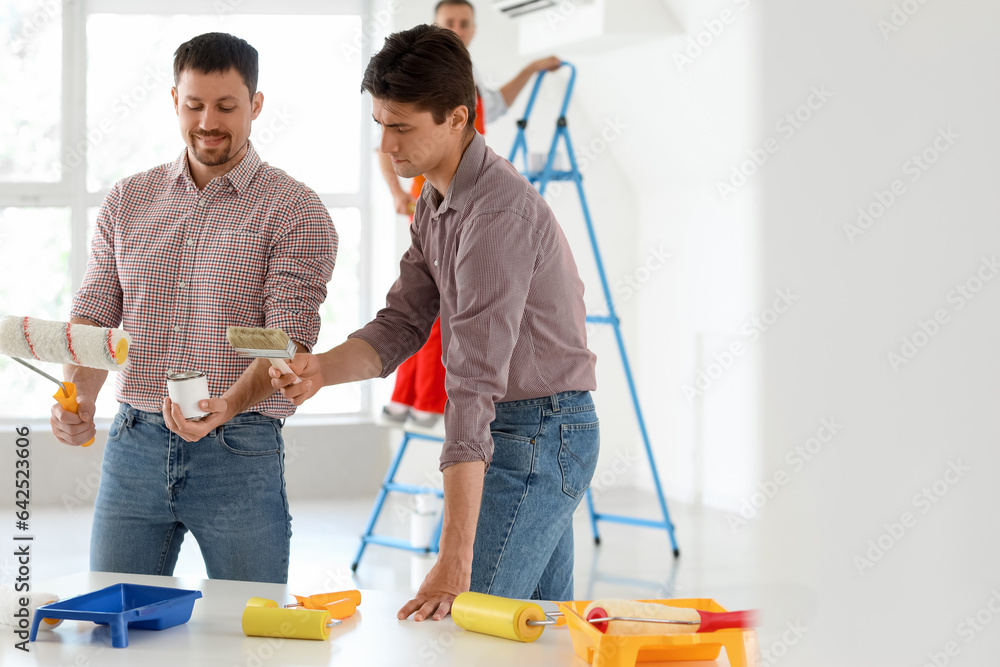 Male builders with paint can and rollers working in room