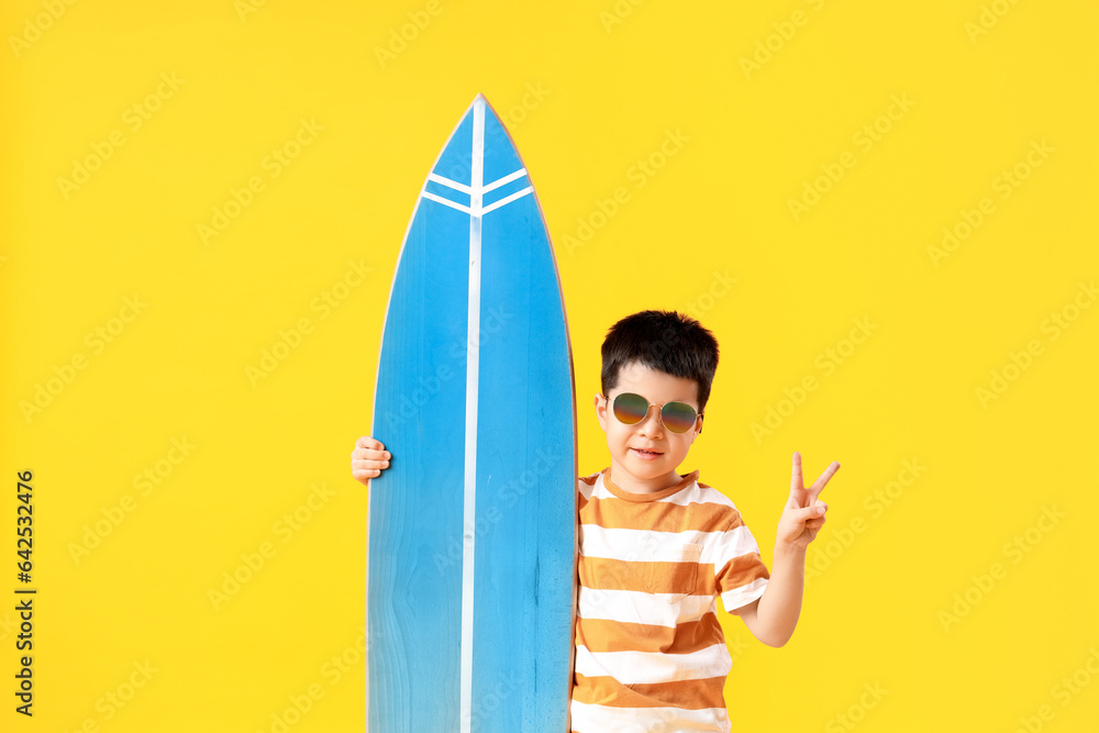Cute little Asian boy with surfboard on yellow background