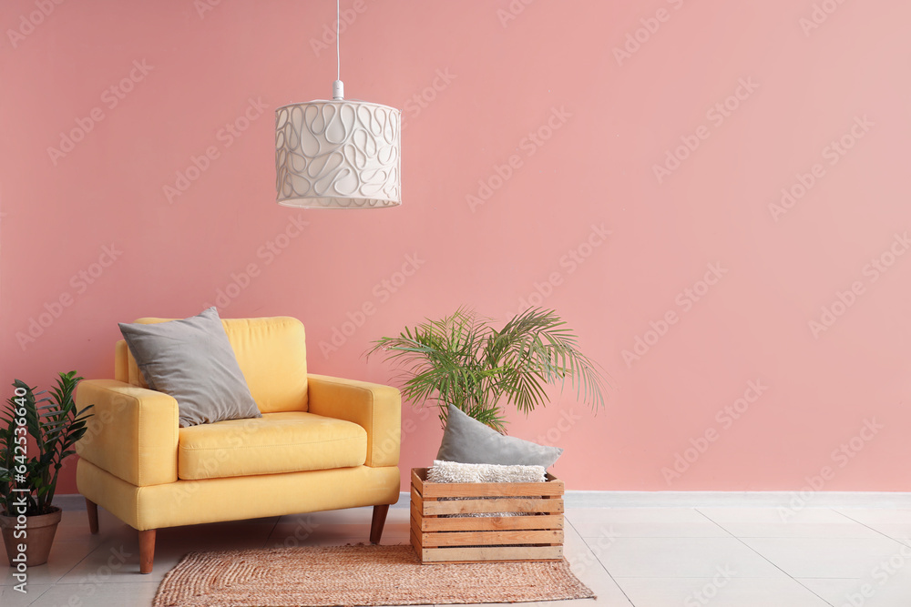 Stylish yellow armchair with cushion and houseplants near color wall