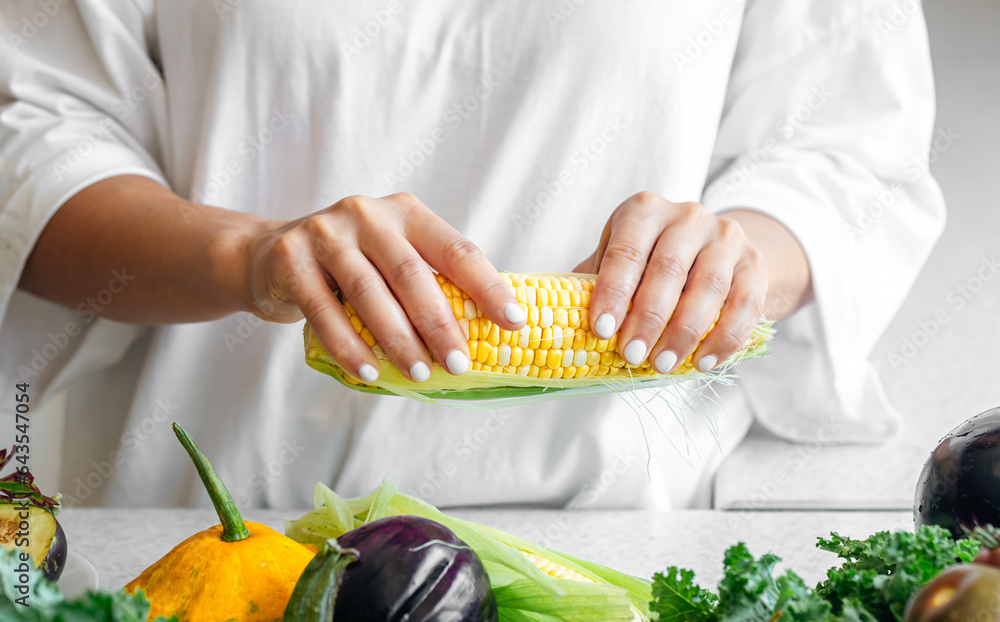 Close-up, raw corn in female hands in the kitchen.