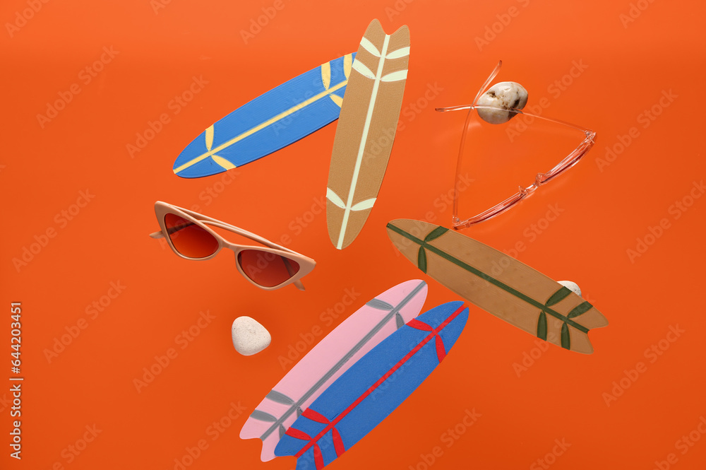 Flying mini surfboards, sunglasses and stones on orange background