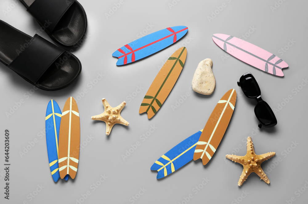 Different mini surfboards, flip-flops, starfishes, stone and sunglasses on grey background