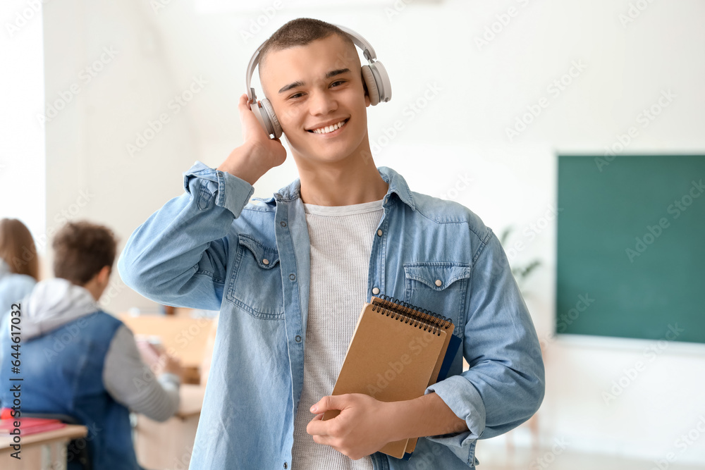 Male student with notebooks listening music in classroom
