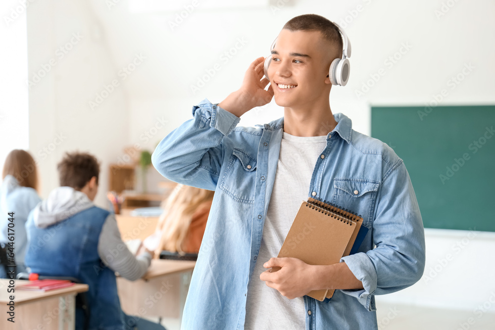 Male student with notebooks listening music in classroom