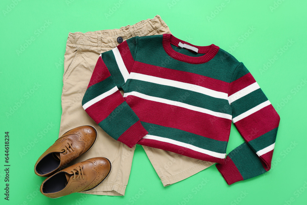 Stylish childrens sweater, pants and shoes on green background