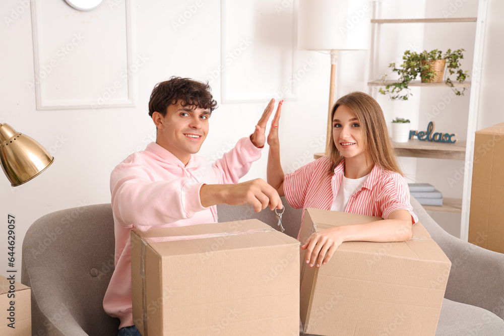Young couple with keys and moving boxes giving each other high-five in their new flat