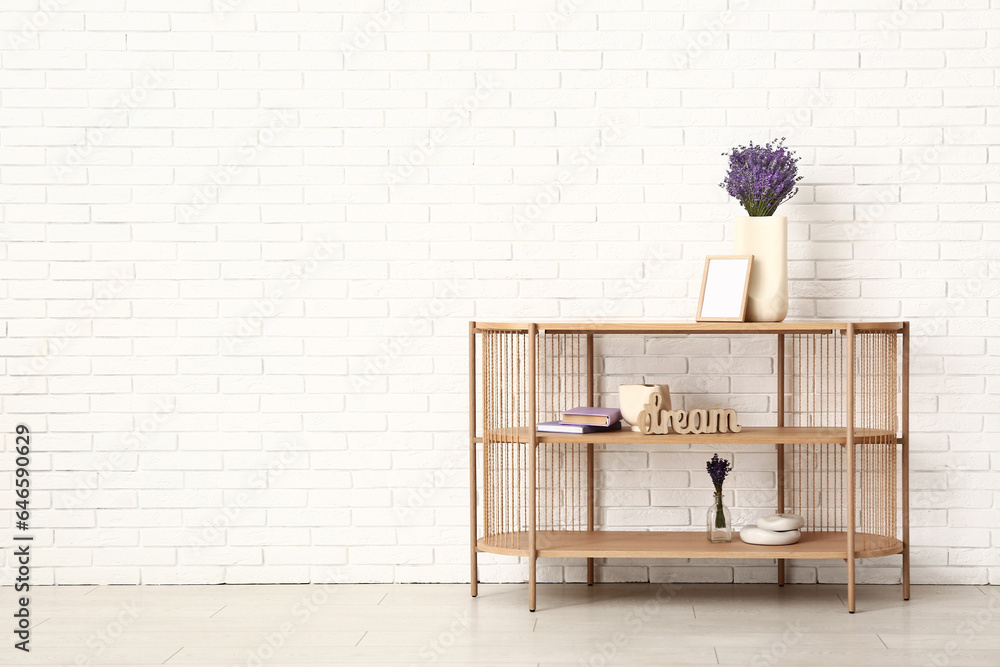 Vase with beautiful lavender flowers and decor on shelving unit near light brick wall in room
