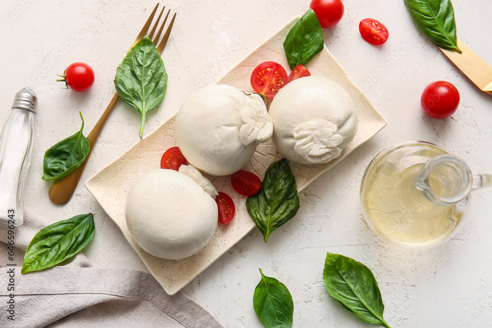 Plate of tasty Burrata cheese with basil and tomatoes on white table