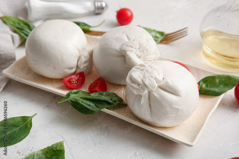 Plate of tasty Burrata cheese with basil and tomatoes on white table