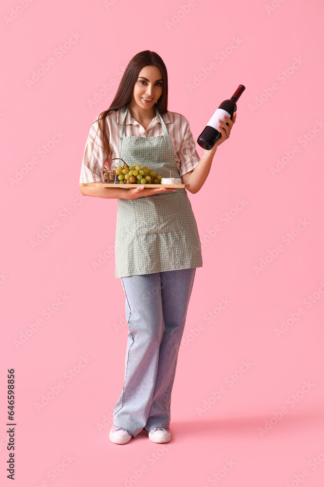 Young woman with bottle of wine and snacks on pink background