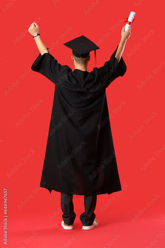 Happy male graduate student with diploma on red background, back view
