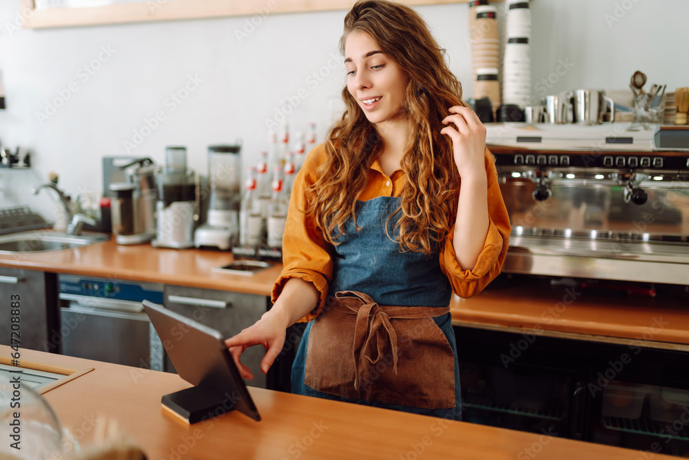 Smiling female barista takes an order from a panchette while standing at the bar counter in a coffee