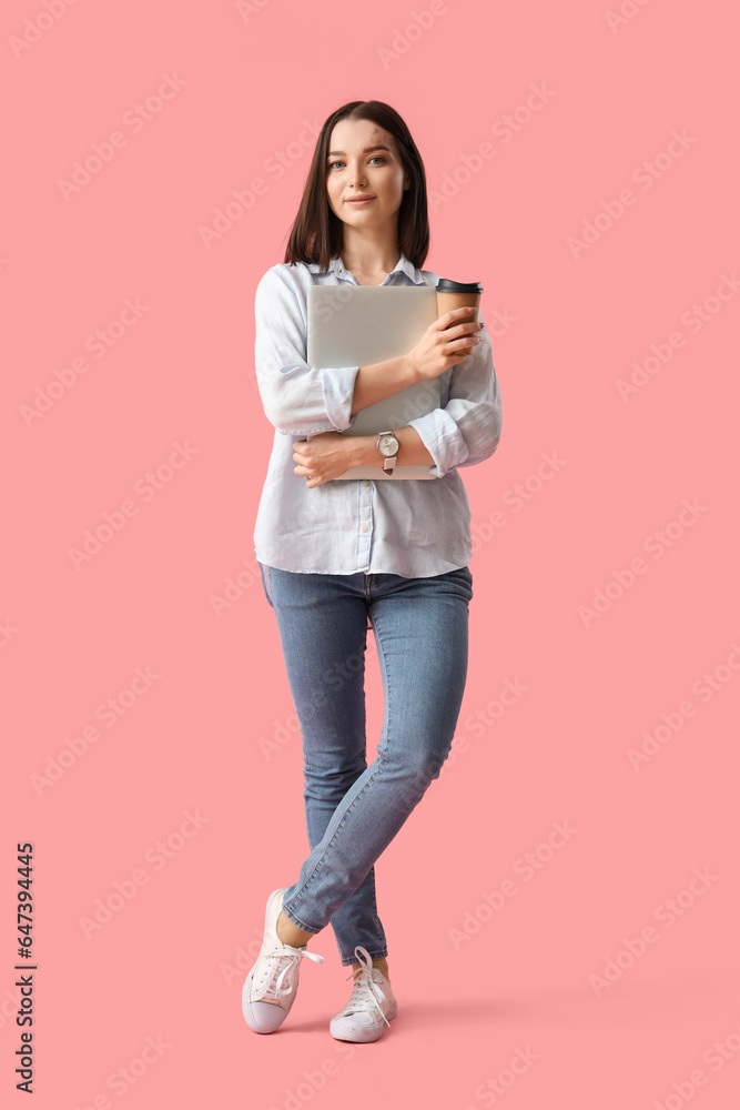 Young businesswoman with cup of coffee and laptop on pink background
