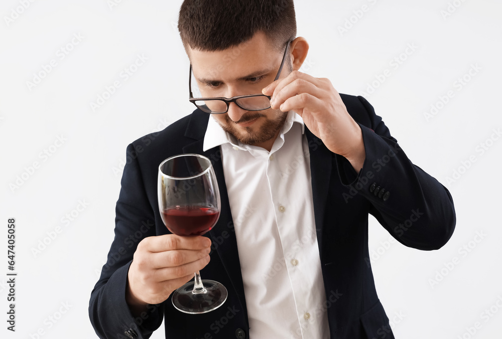 Young sommelier with glass of wine on grey background