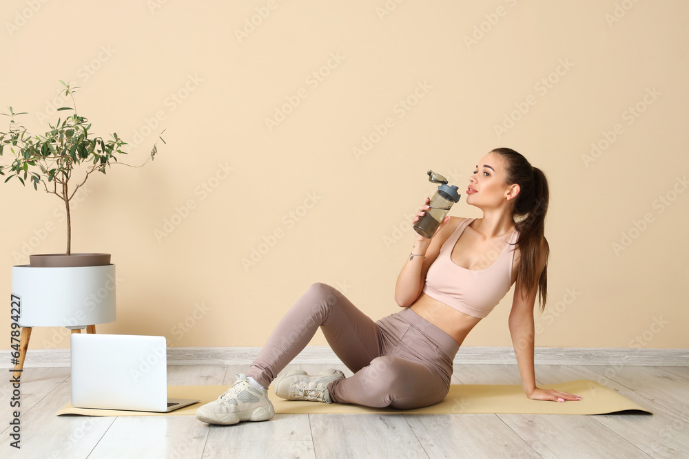 Sporty young woman with bottle of water training at home