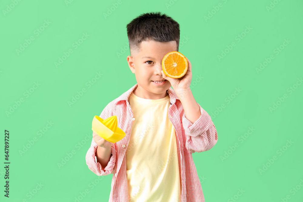 Little Asian boy with juicer and fresh orange slice on green background