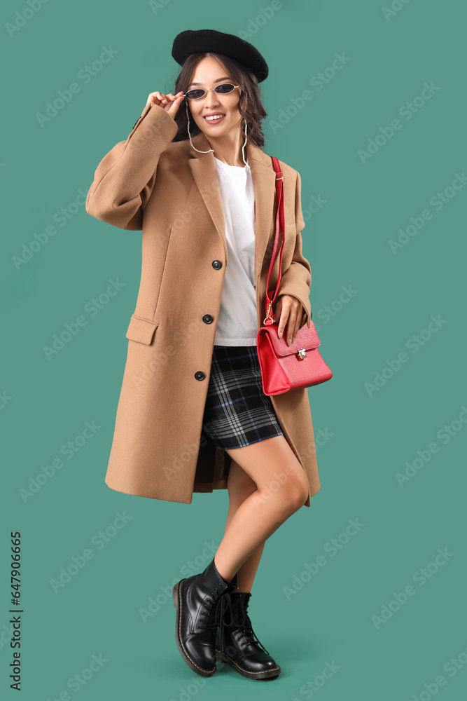 Stylish young Asian woman in fall clothes on green background