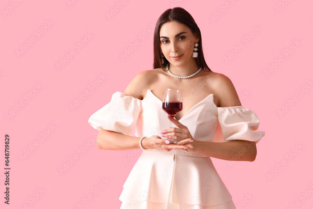 Young woman with glass of wine on pink background