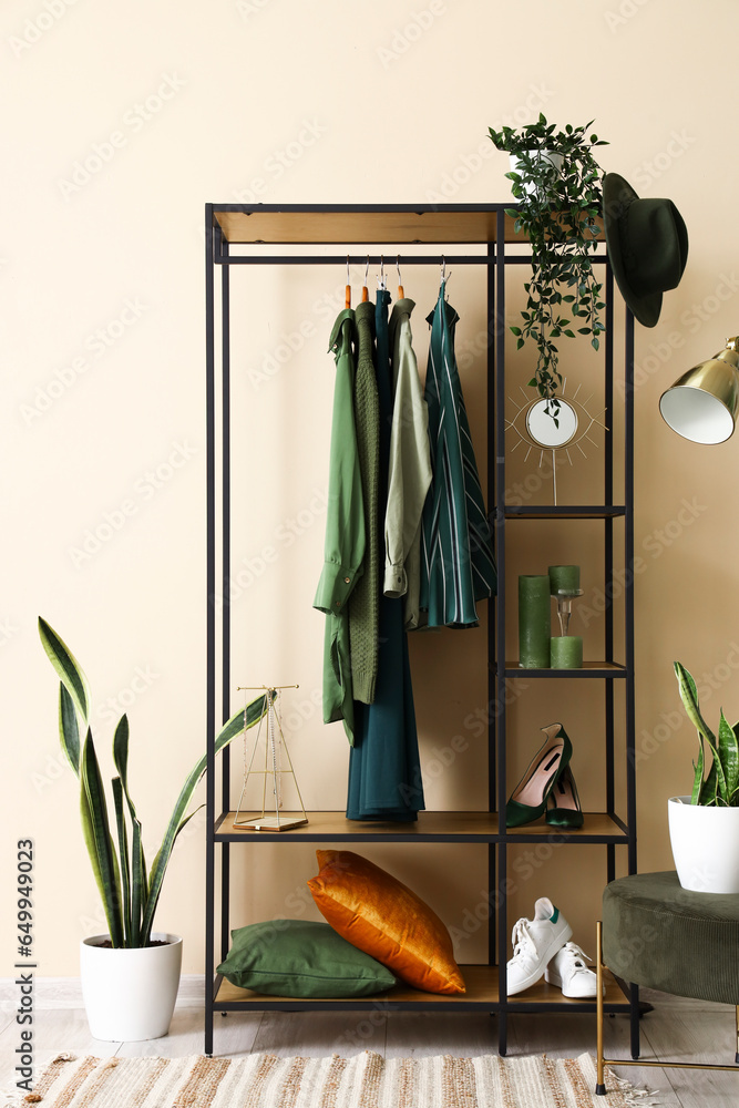 Shelving unit with clothes and shoes near beige wall in hall