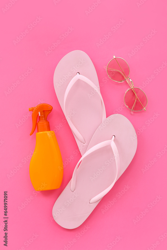 Pair of flip flops with sunscreen spray and sunglasses on pink background