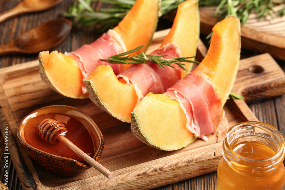 Board of tasty melon with prosciutto and honey on wooden table, closeup