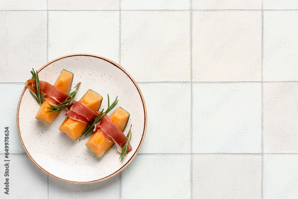 Plate of tasty melon with prosciutto and rosemary on light tile background