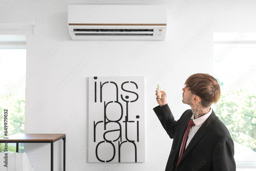 Young businessman turning on air conditioner in office