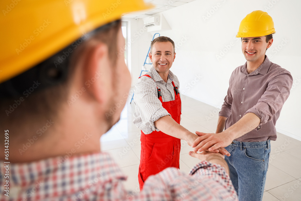 Team of male builders putting hands together in room