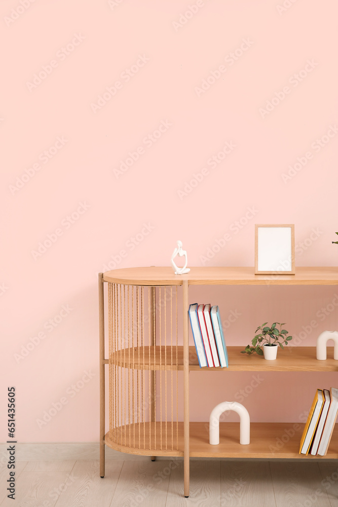 Bookshelf with houseplant near pink wall in room