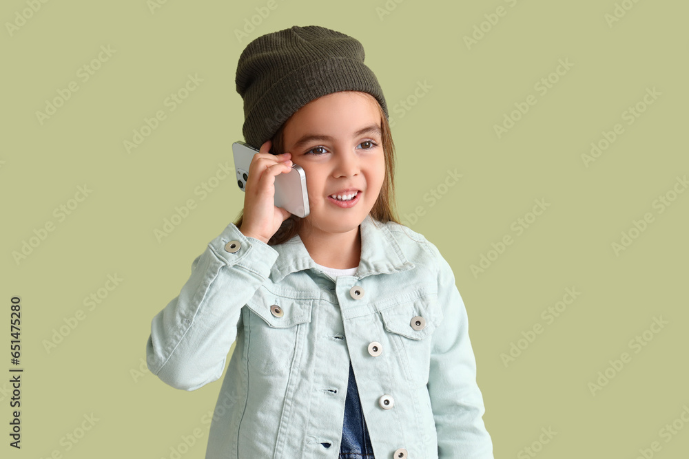 Cute little girl in hat talking by mobile phone on green background