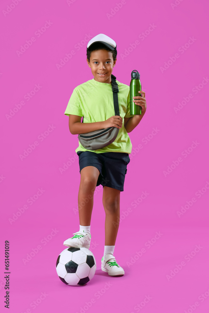 African-American little boy with bottle of water and soccer ball on purple background