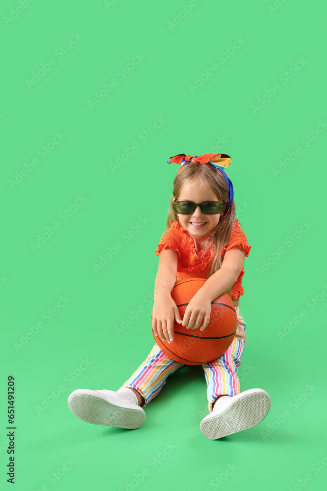 Cute little girl with ball sitting on green background