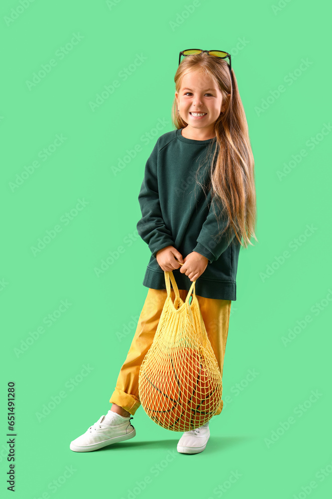Cute little girl with ball in string bag on green background