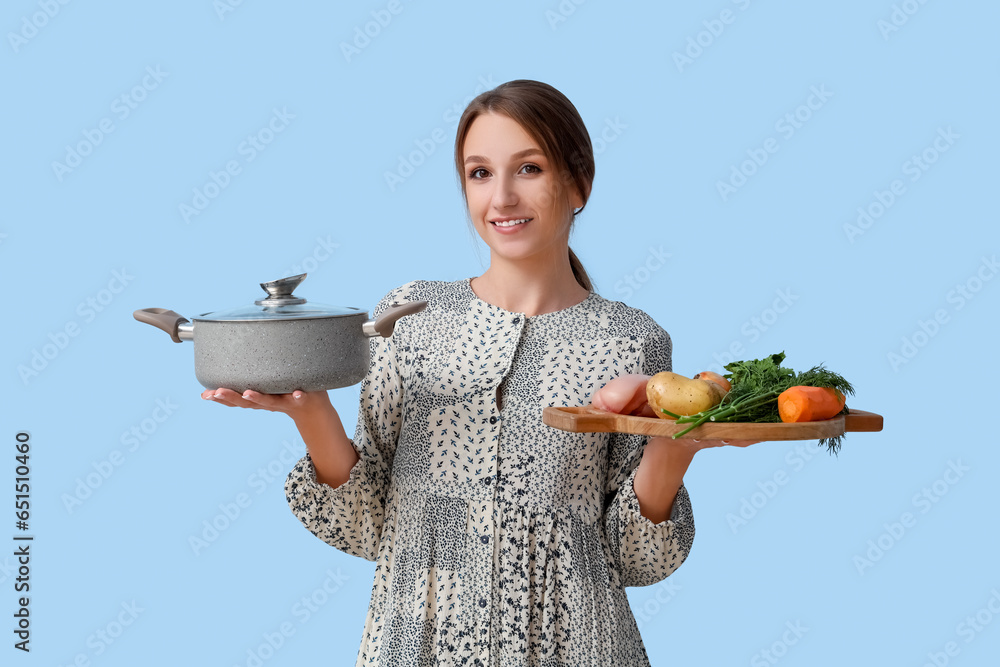 Young woman with pot and ingredients for chicken soup on blue background
