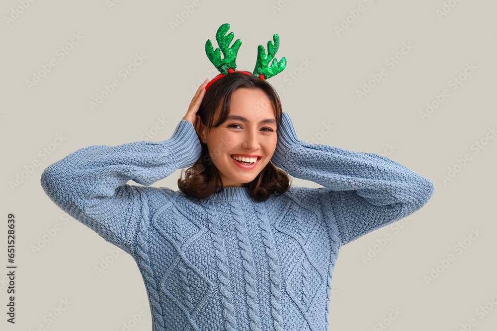 Young woman in reindeer horns and warm sweater on light background