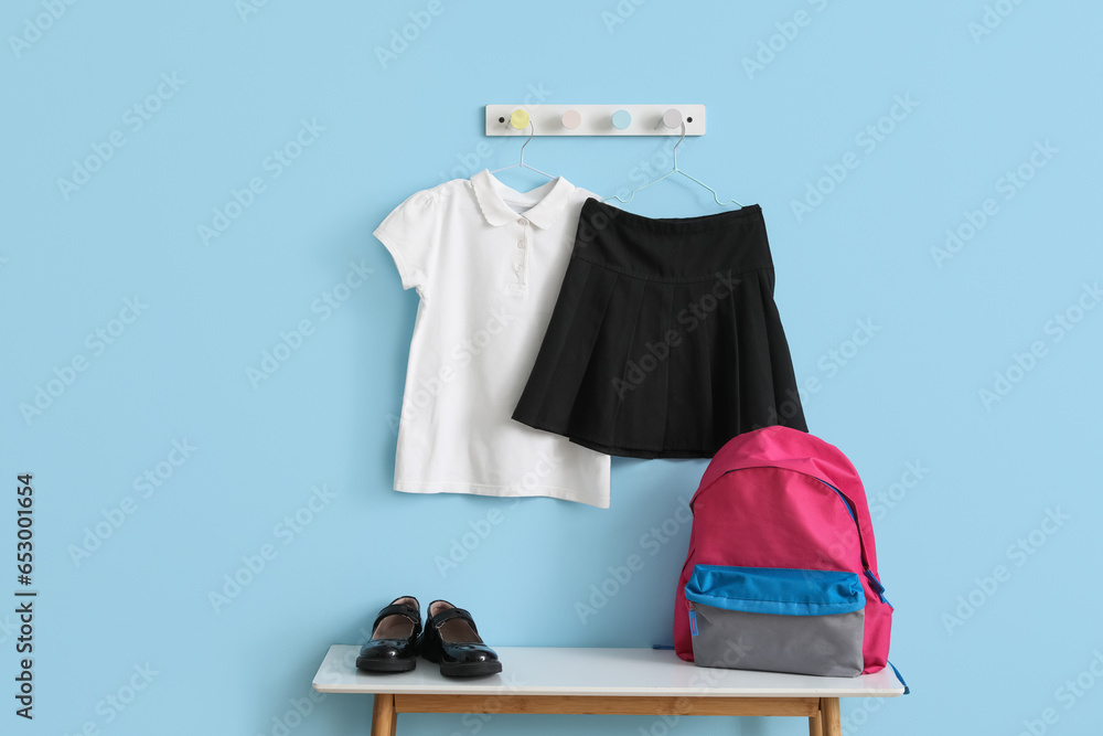 Table with backpack, shoes and stylish school uniform hanging on blue wall in room